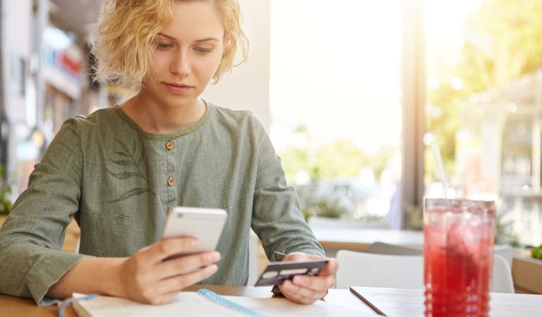 Businesswoman with stylish hairdo paying with credit card while shopping online using mobile